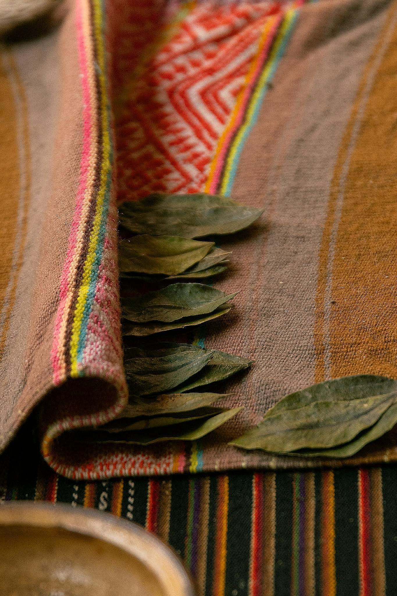 Colorful handwoven textile from Cusco, Peru, with coca leaves, showcasing traditional patterns.