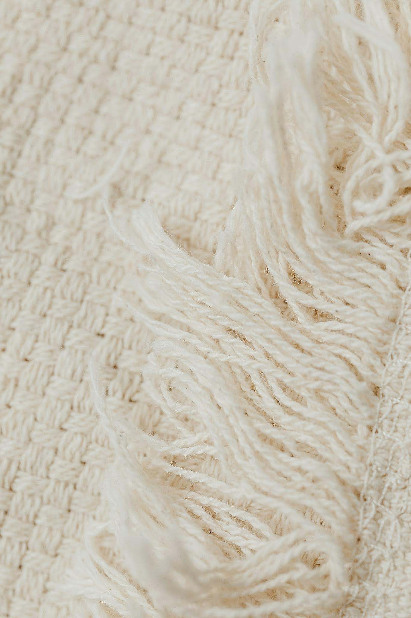 Detailed close-up view of woven cream wool fabric with fringe edges.