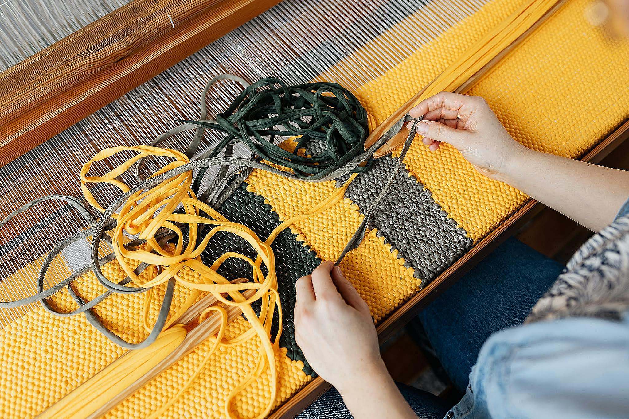 Top view of crop anonymous female employee working on wooden weaving loom machine with stretched durable colorful threads in workshop