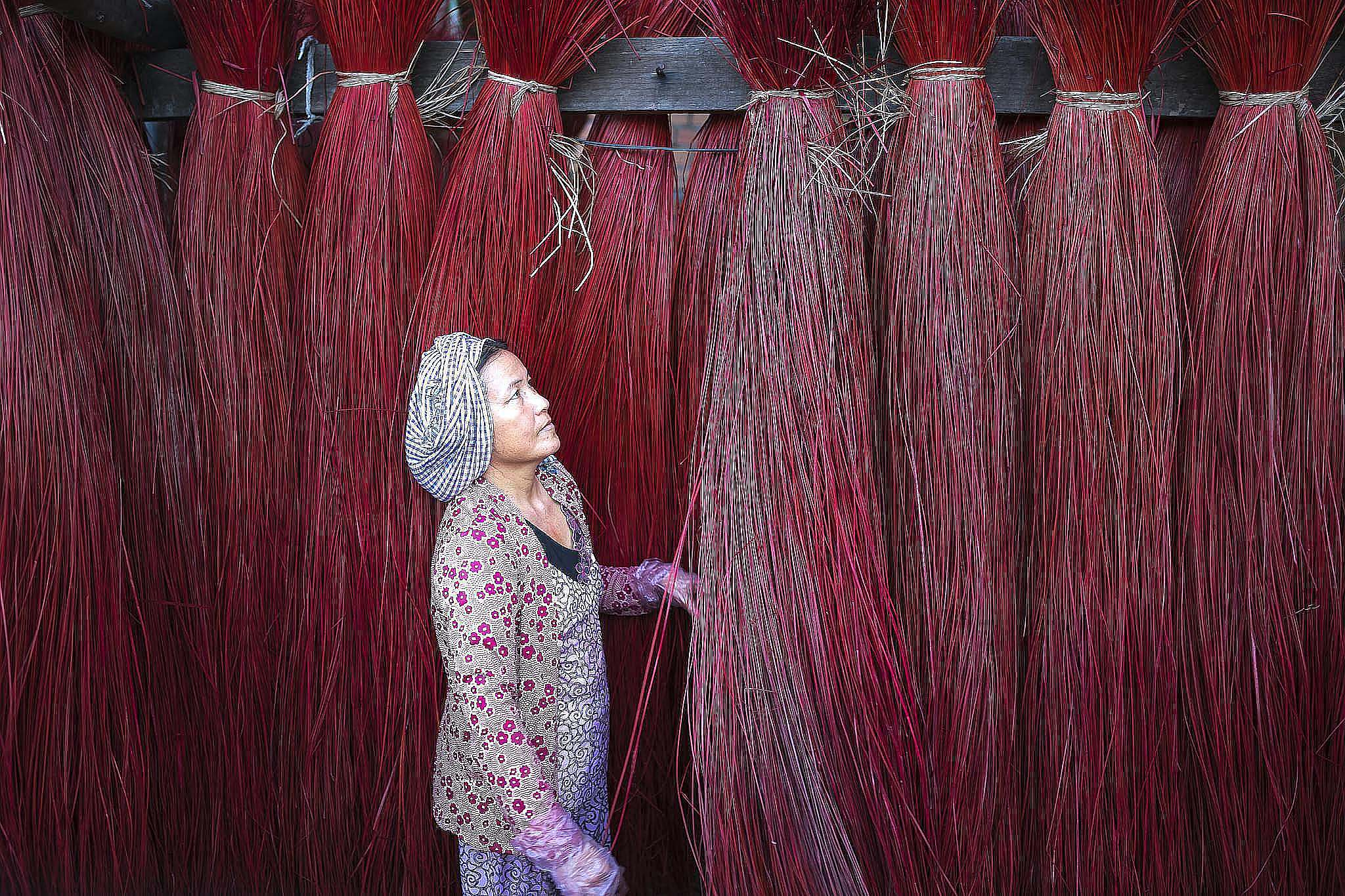 Woman observing vibrant red straw bundles in traditional setting, showcasing textile craft.